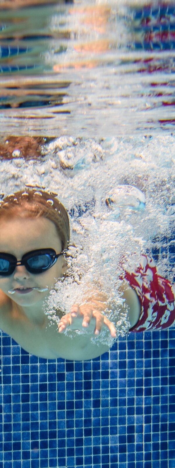 Das Foto zeit einen tauchenden Jungen in Badehose und mit Schwimmbrille. 